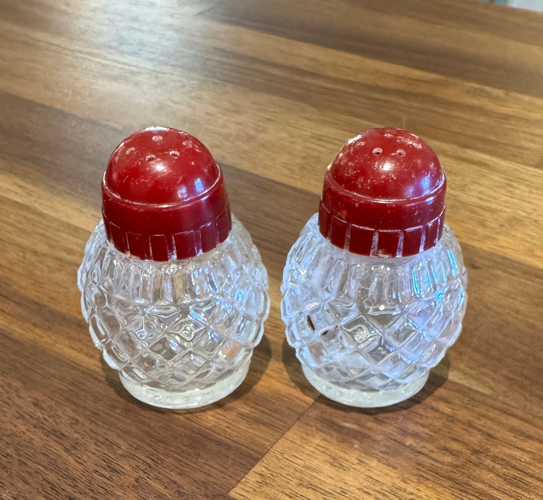 Two small clear glass bottles with textured bodies and red screw-top lids, placed on a wooden tabletop.